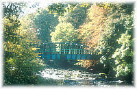 Almondell Country Park - a sunny picture of the sparkling river bordered by trees in autumn colours and spanned by an old iron footbridge